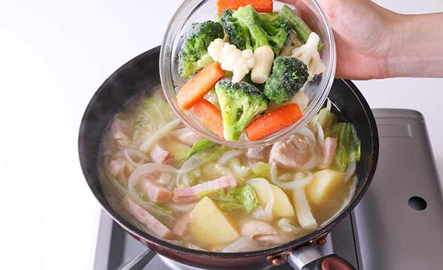 べーコンや野菜を加えた鍋に冷凍野菜ミックスを加えている写真