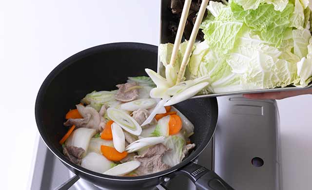肉・白菜の芯・にんじんを炒めているフライパンに長ねぎ・きくらげ・白菜の葉を加えている写真